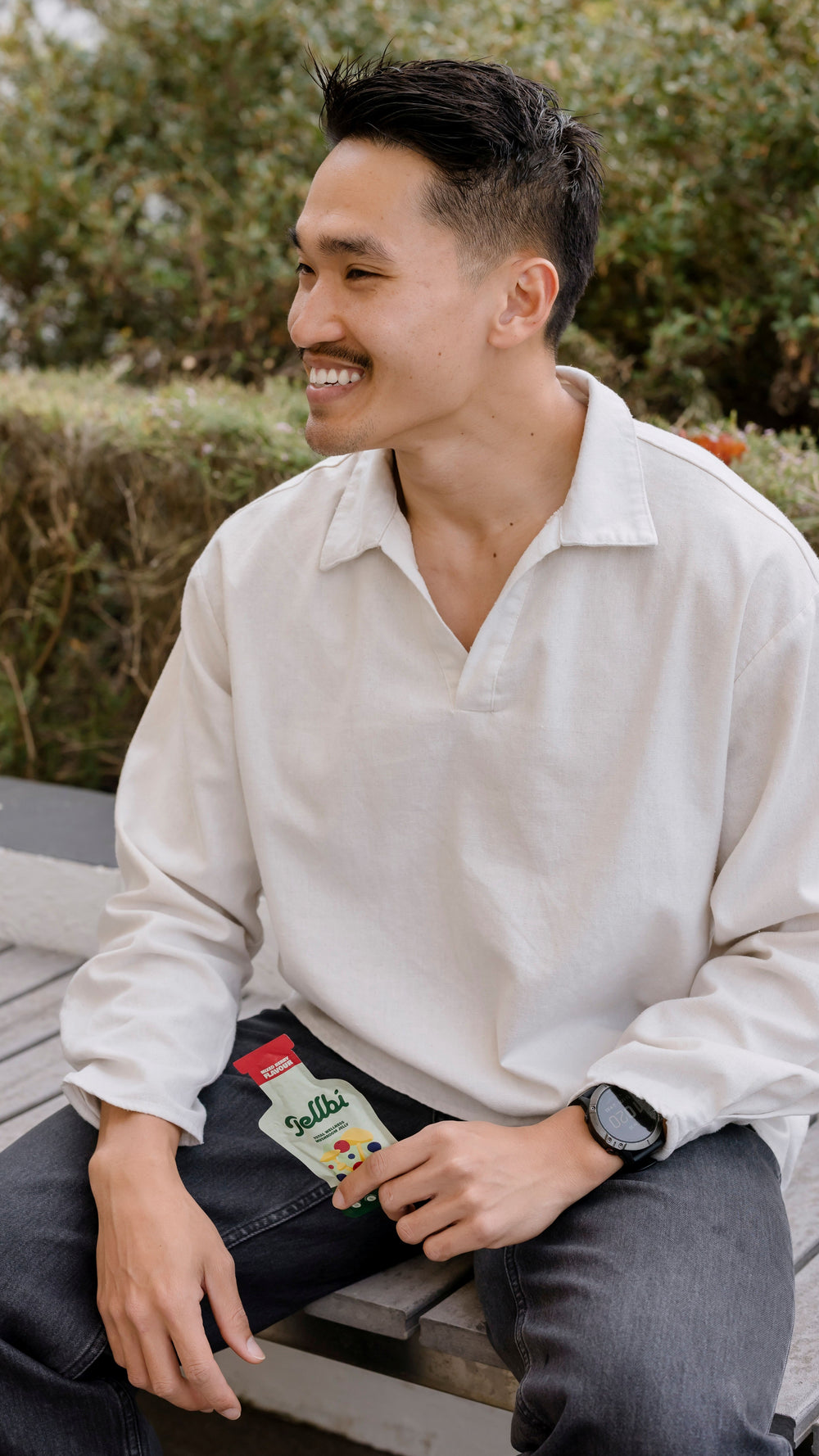 Man sitting outdoors wearing a white shirt with a visible brand label.